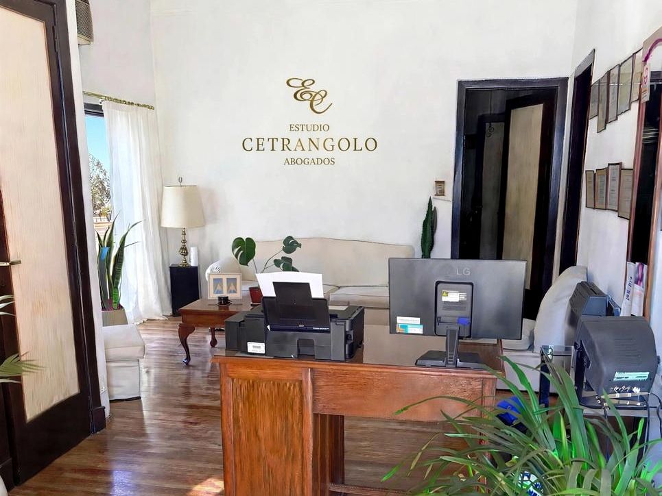 Recepción del Estudio Cetrángolo en San Martín 881, Luján: el monograma del estudio en la pared, sillón de espera y escritorio de entrada.